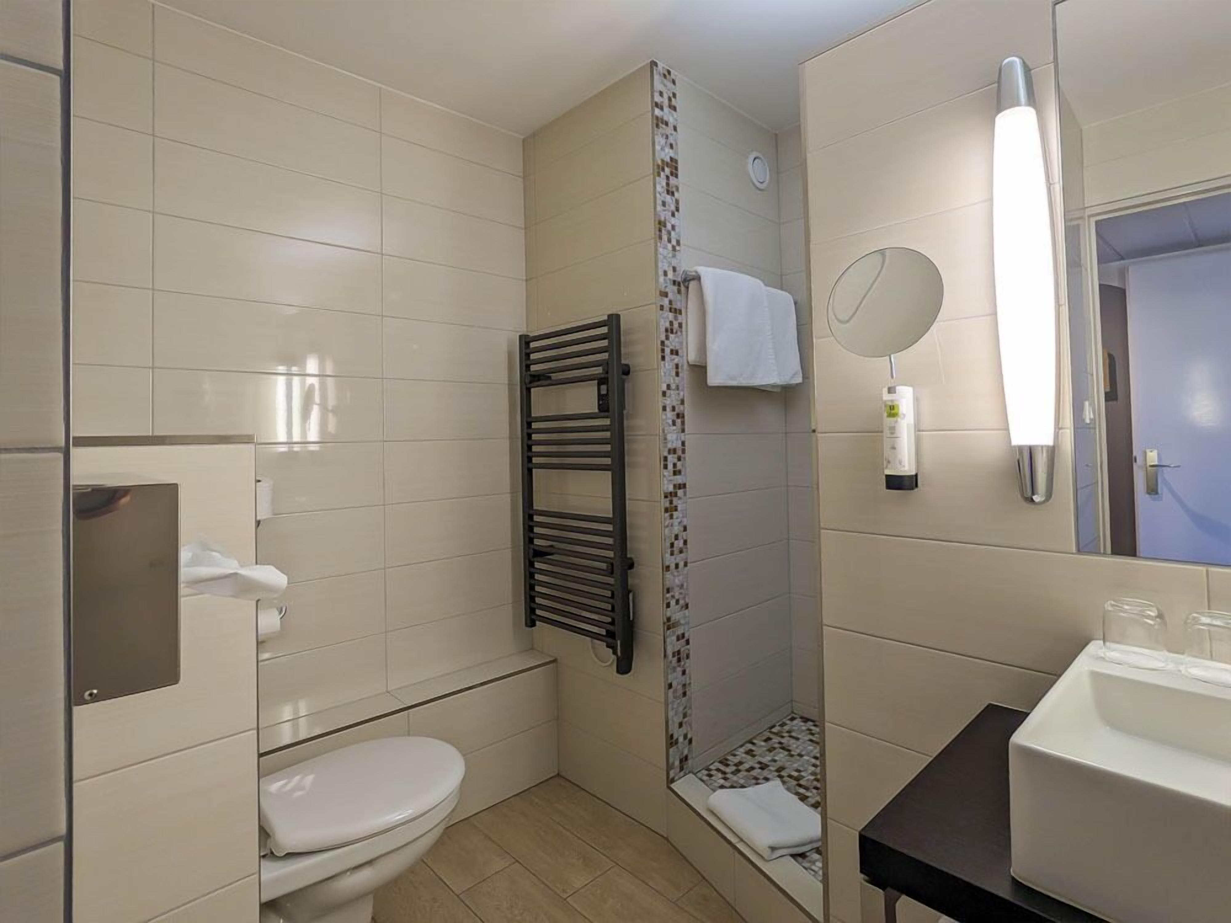 A bathroom with a toilet, a shower, a towel rack, a mirror, and a sink.