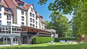A hotel with a large building, a covered outdoor area, and a well-maintained lawn with lounge chairs. - Hotel Restaurant & Spa Verte Vallée (Munster)