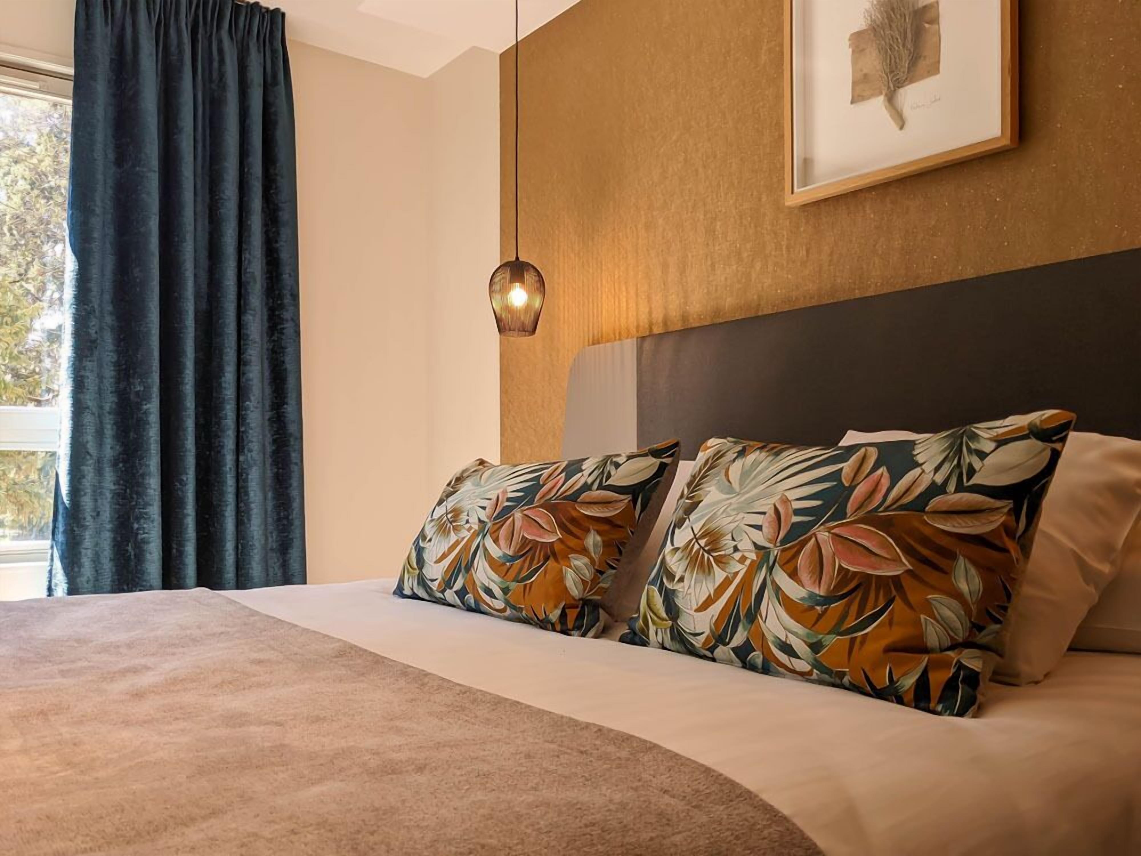 A bed with floral-patterned pillows, a hanging light fixture, and a framed picture on the wall.