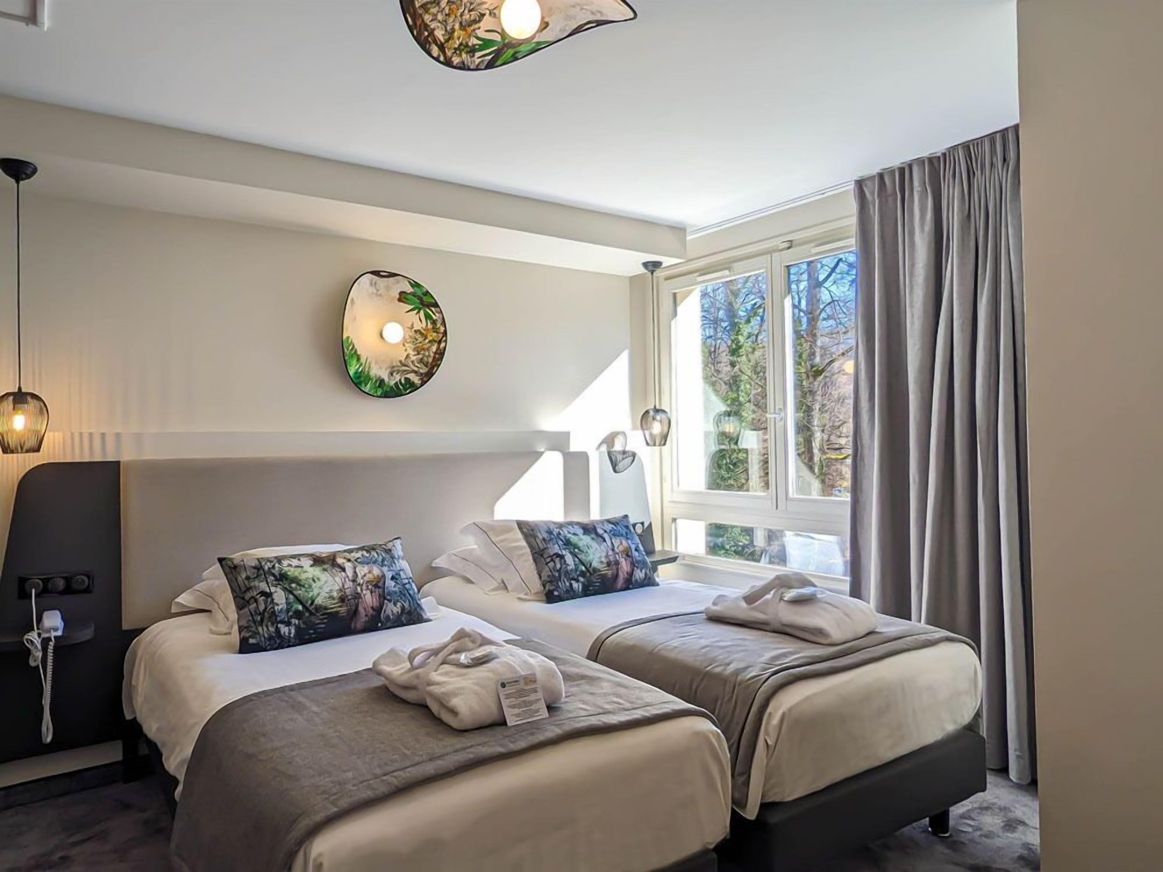 Quarto de hotel com duas camas, uma janela ampla, uma obra de arte na parede e um telefone na mesa de cabeceira.