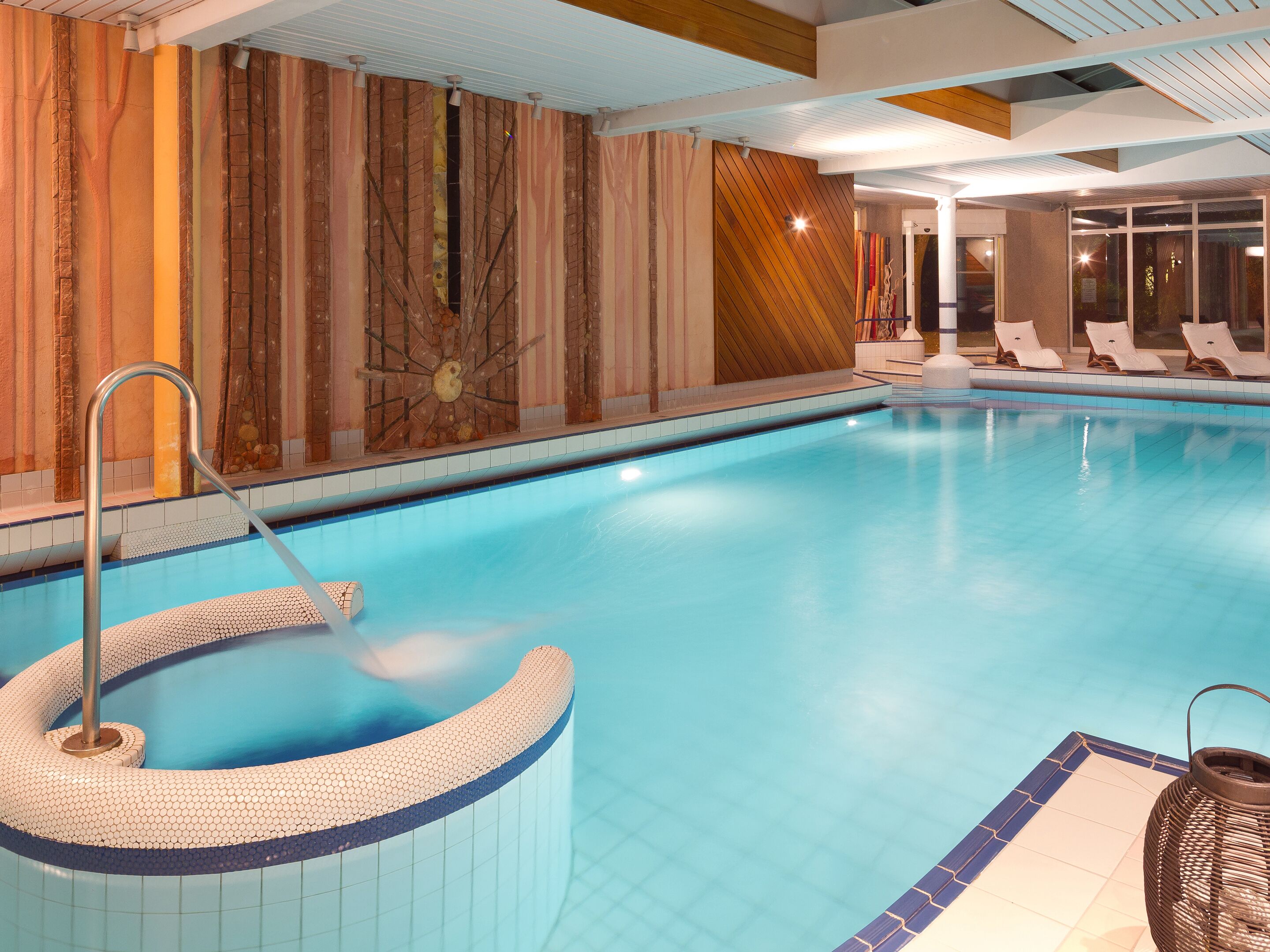En swimmingpool med et spa, liggestole og en dekorativ væg.