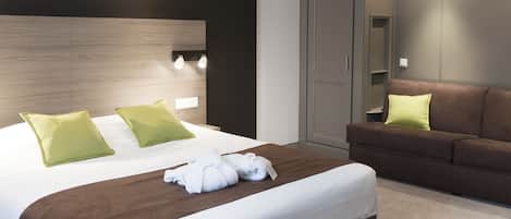 A modern hotel room with a large bed, a brown sofa, and a wardrobe.