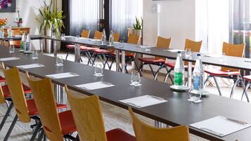 Une salle de conférence avec de longues tables, des chaises rouges et des bouteilles d’eau.