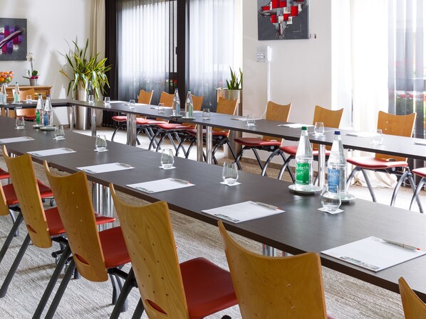 A conference room with long tables, red chairs, and water bottles.