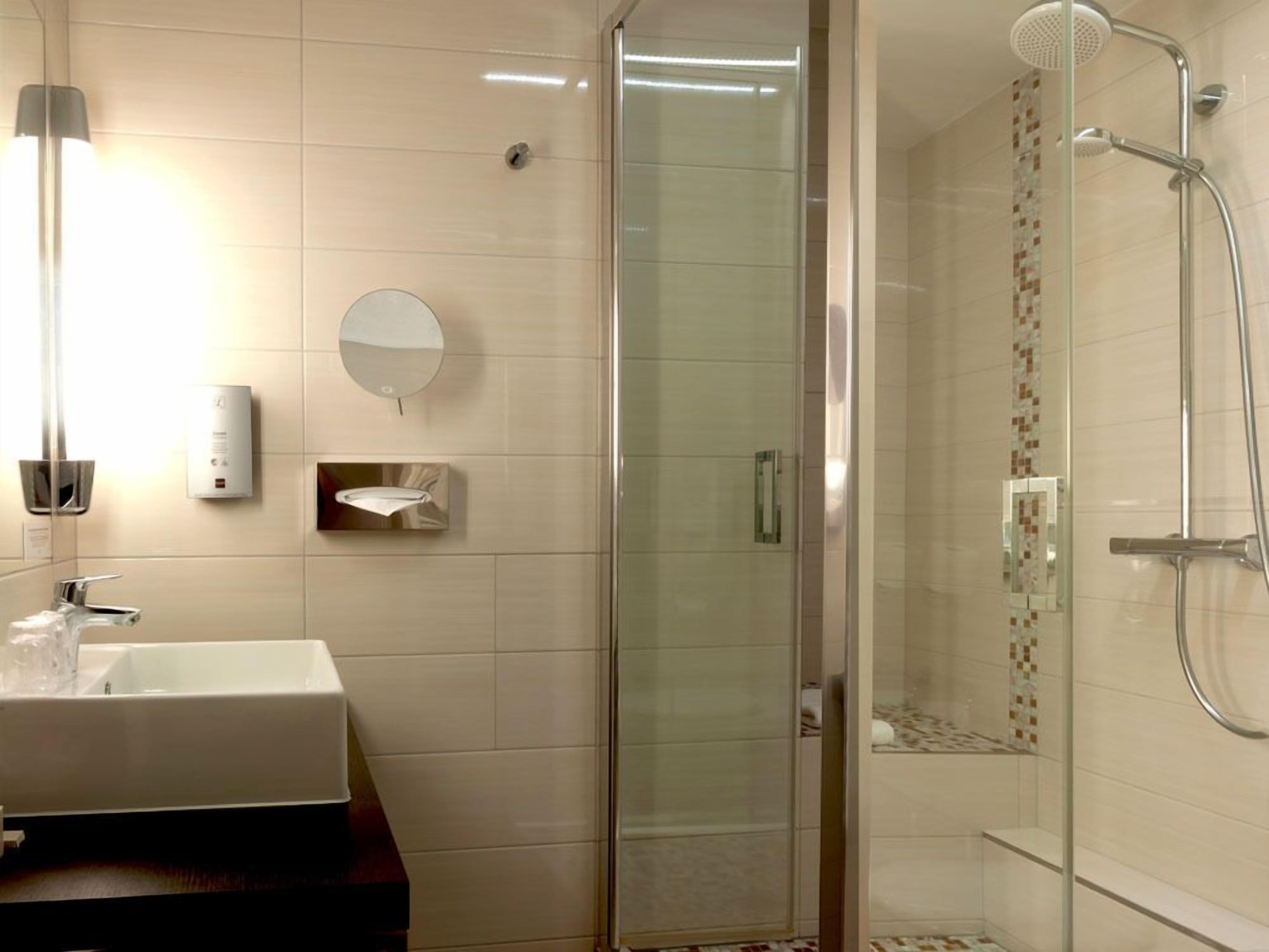 A modern bathroom with a glass-enclosed shower, a white sink, and a mirror.