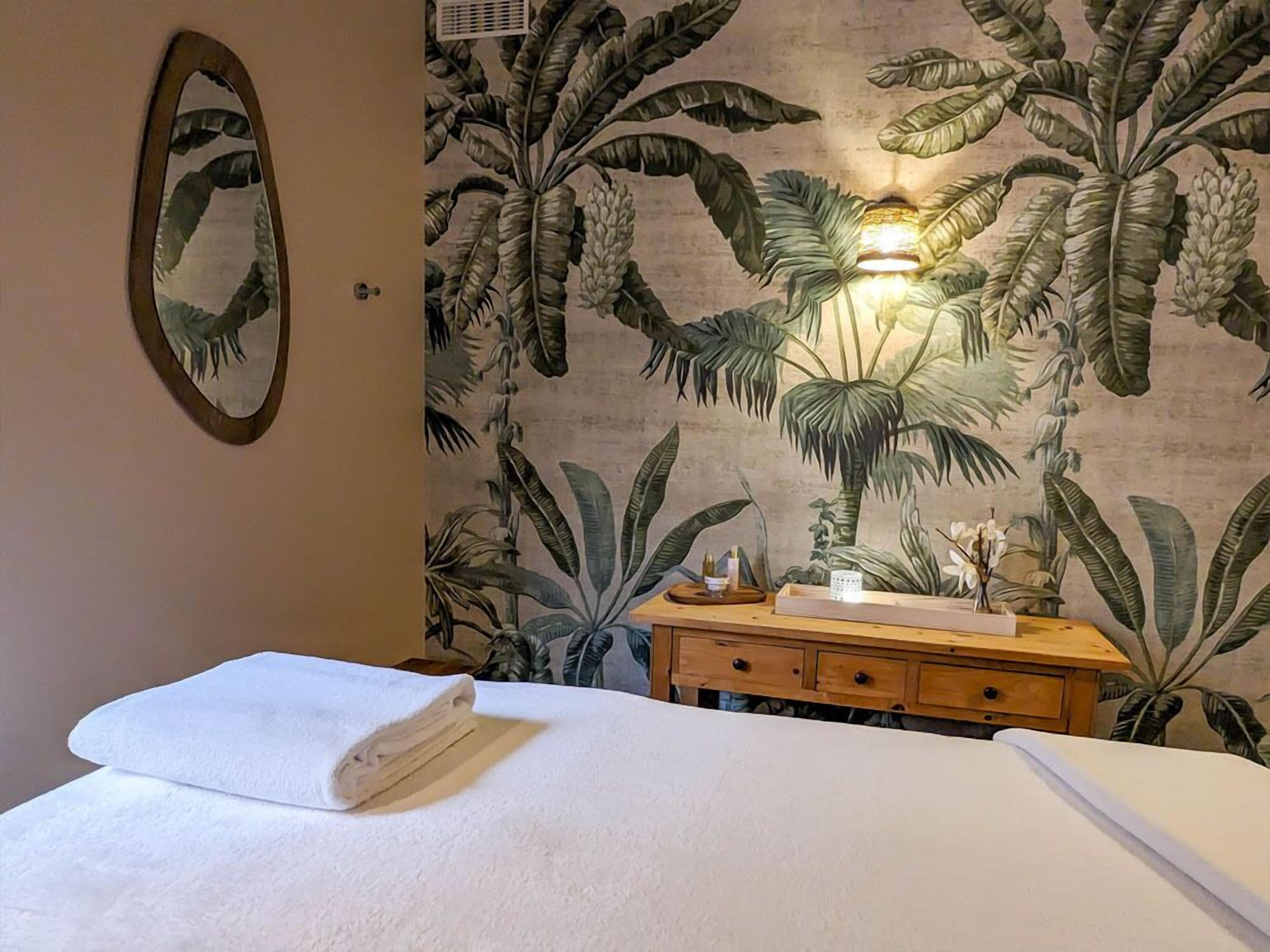 Habitación de hotel con una cama, un aparador de madera, un espejo y un mural de plantas tropicales en la pared.