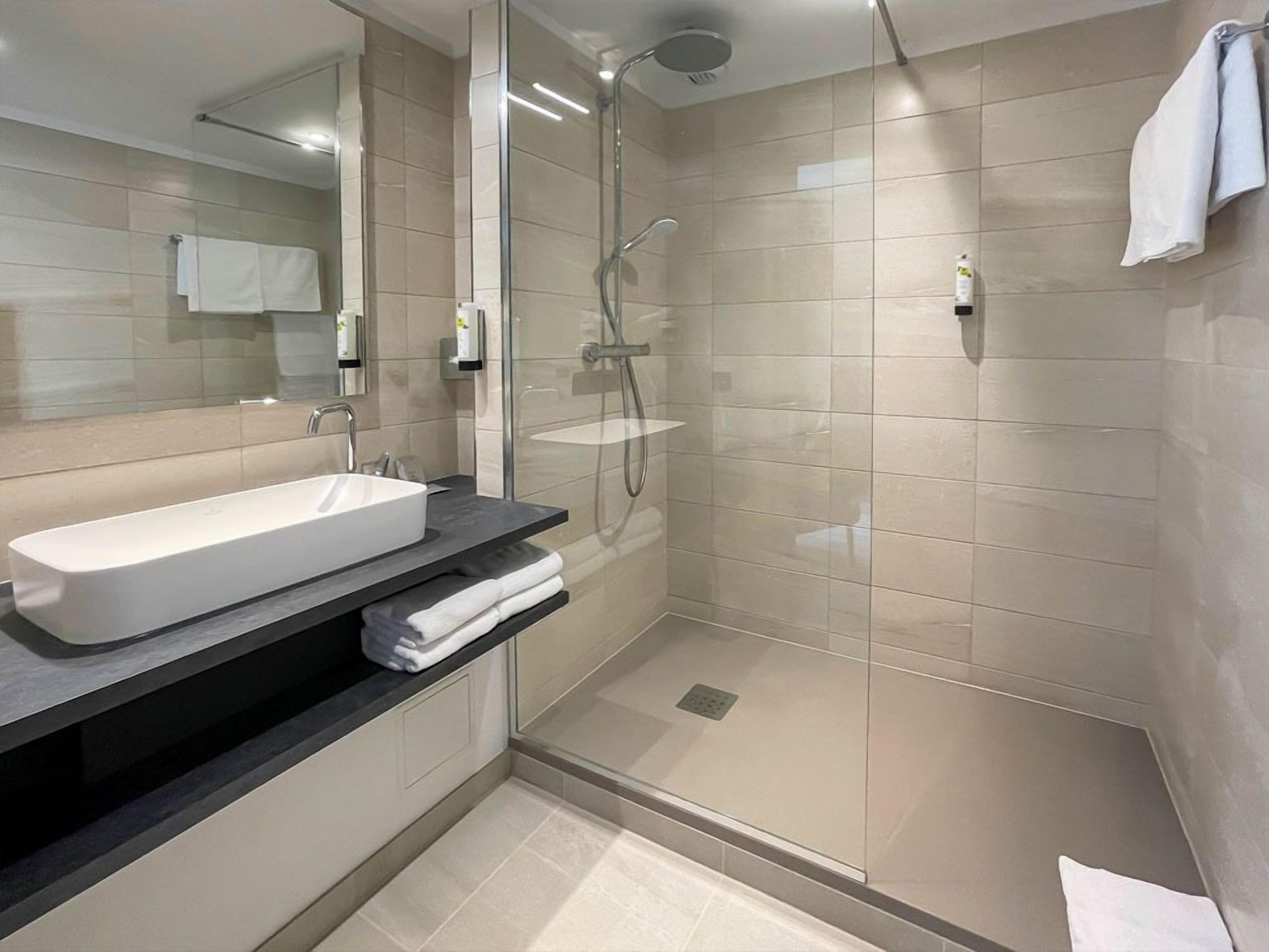 Une salle de bain moderne avec une douche à parois de verre, un lavabo blanc et un miroir.