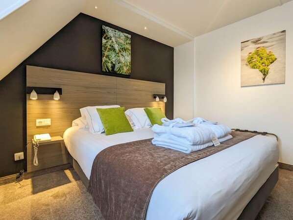 A modern bedroom with a sloped ceiling, a wooden headboard, a large bed with white and green pillows, and two wall-mounted lamps.