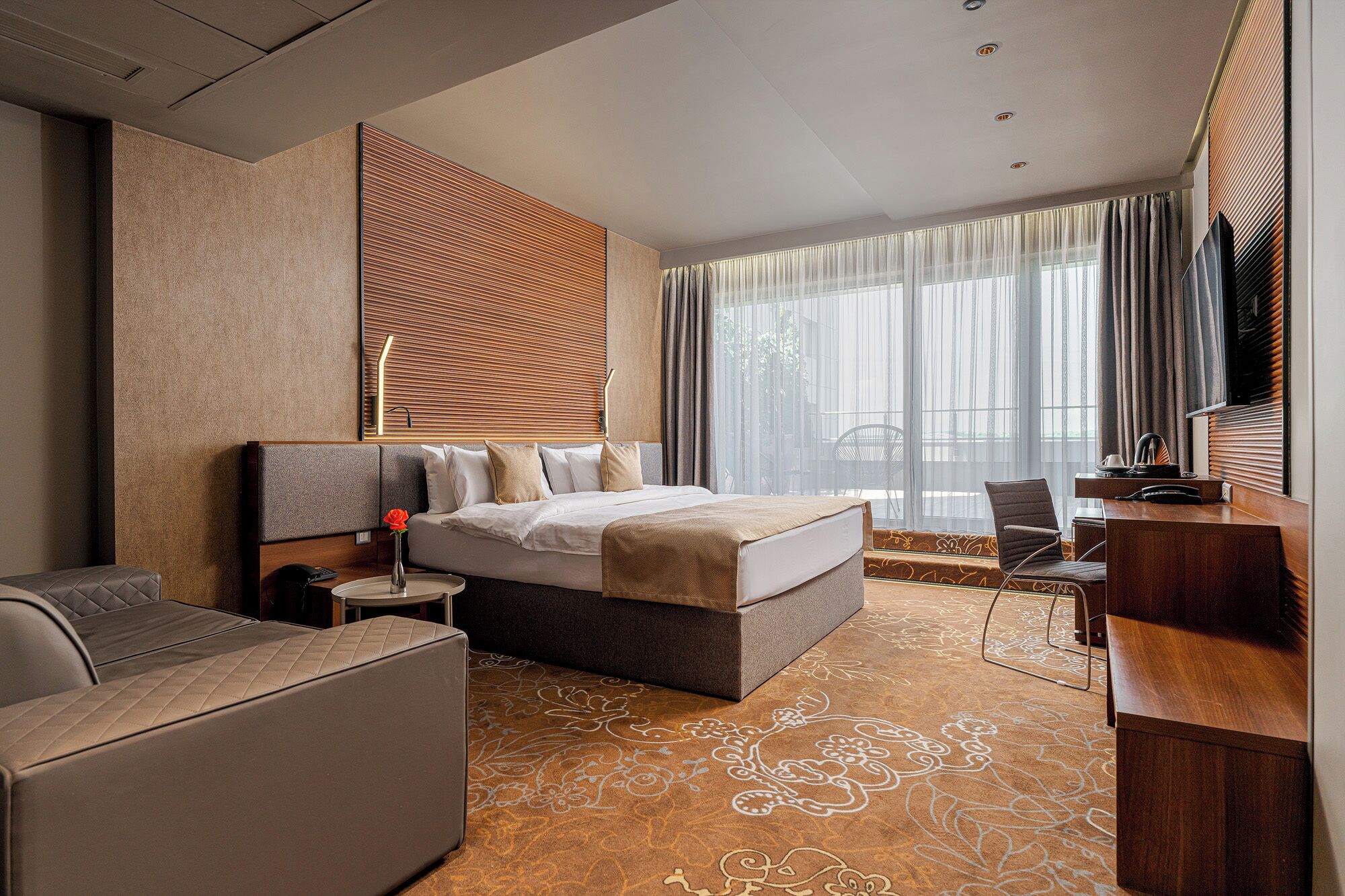 A modern hotel room with a large bed, a desk, and a seating area.
