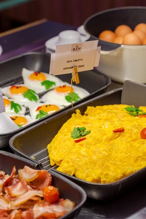 A breakfast buffet with scrambled eggs, bacon, and a sign indicating 'OUA OMLETA SCRAMBLED EGGS'.