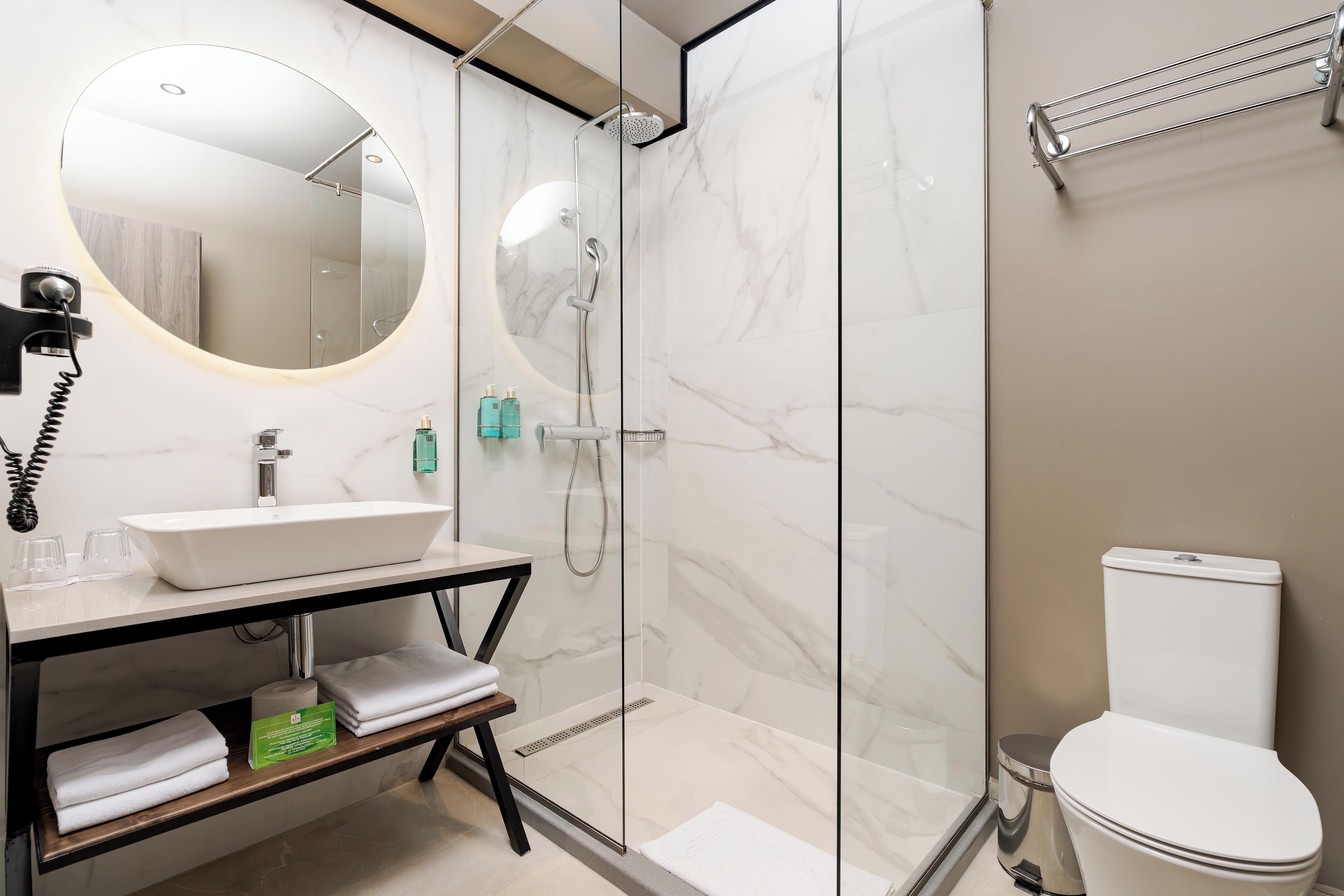 Un baño moderno con ducha envuelta en vidrio, un lavamanos blanco y un inodoro.