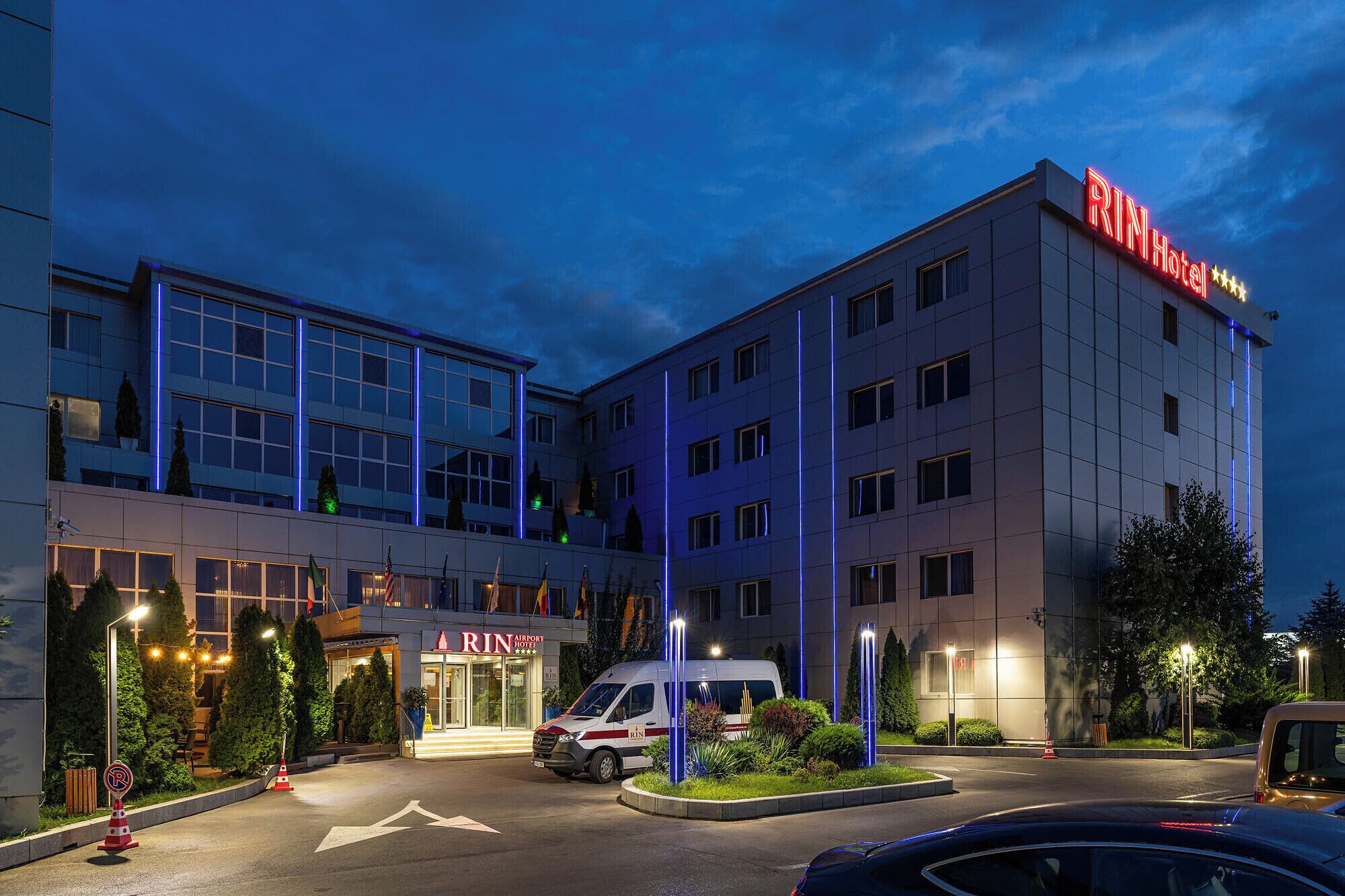 A hotel with a modern design, featuring a prominent 'RIN' sign, a parking area, and a van parked in front.