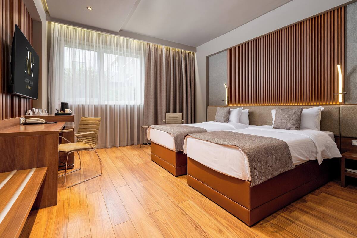 A modern hotel room with two beds, a desk, and a TV.