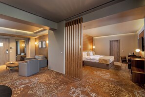 A hotel room with a bed, a seating area with sofas, a desk, and a large window.