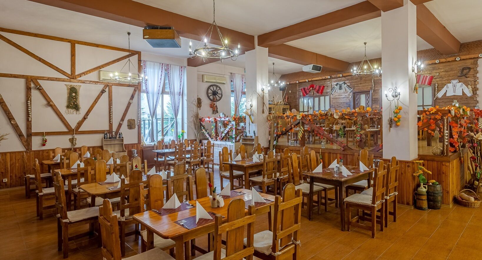 A restaurant with wooden tables and chairs, a chandelier, and autumn decorations.