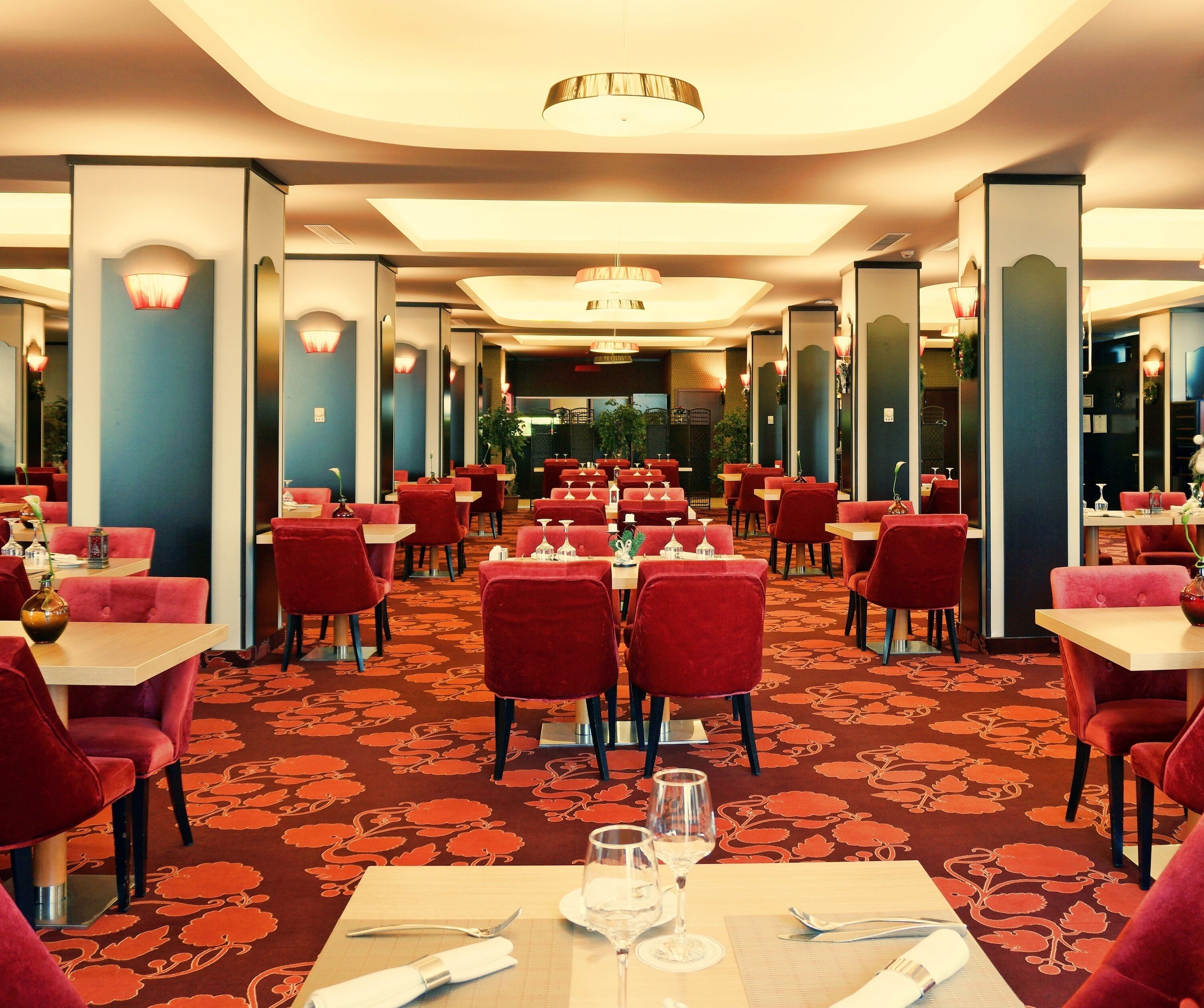 Un restaurant spacieux avec des chaises à revêtement rouge, des tables blanches et un tapis à motifs.