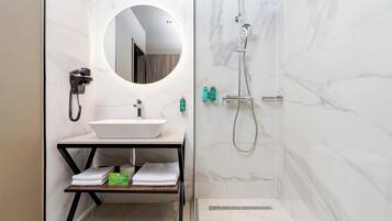 A modern bathroom with a white marble sink, a round mirror, a handheld shower, and a towel rack.