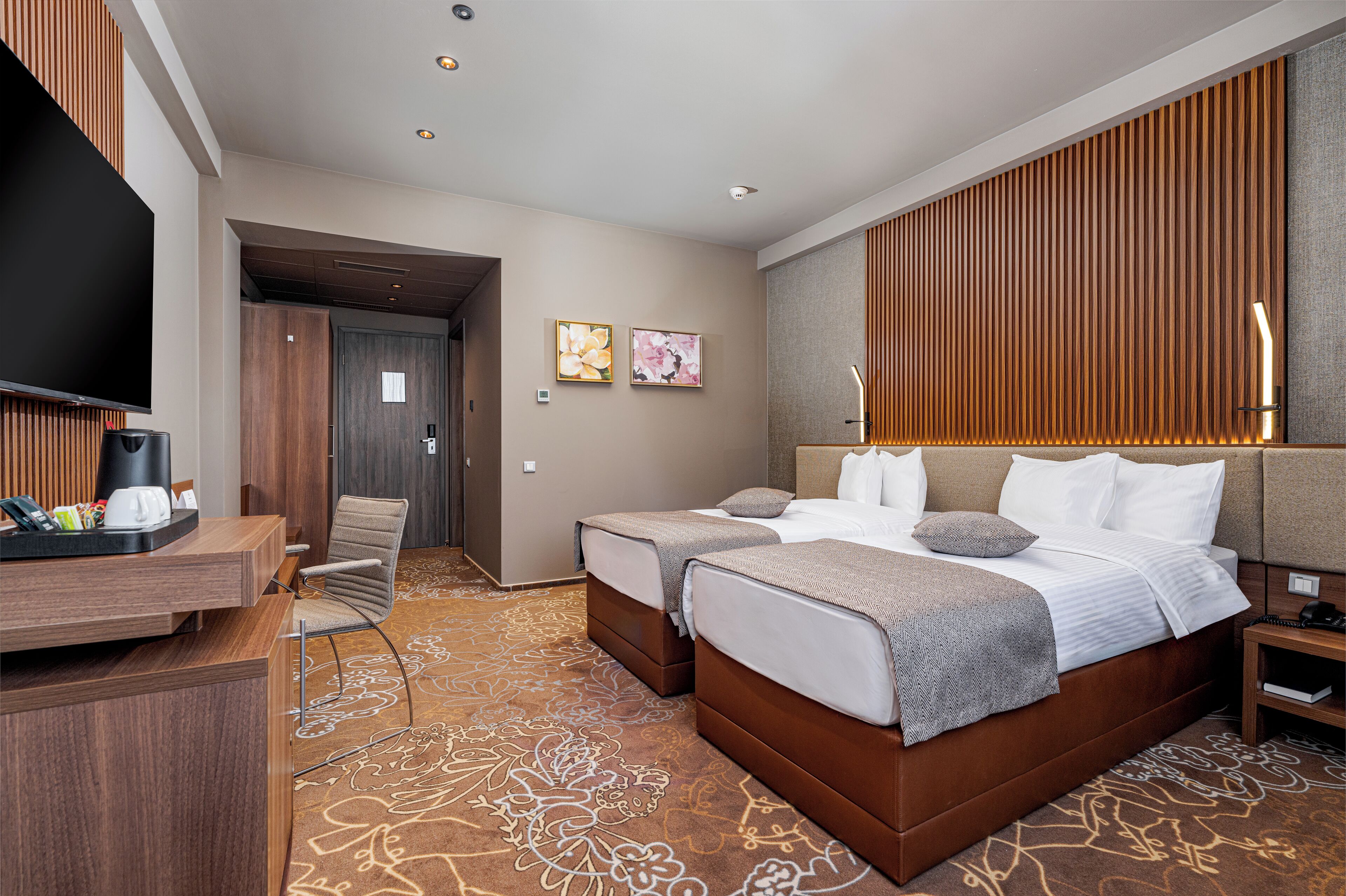 Habitación de hotel con dos camas, un escritorio, un televisor y un panel de pared de madera.