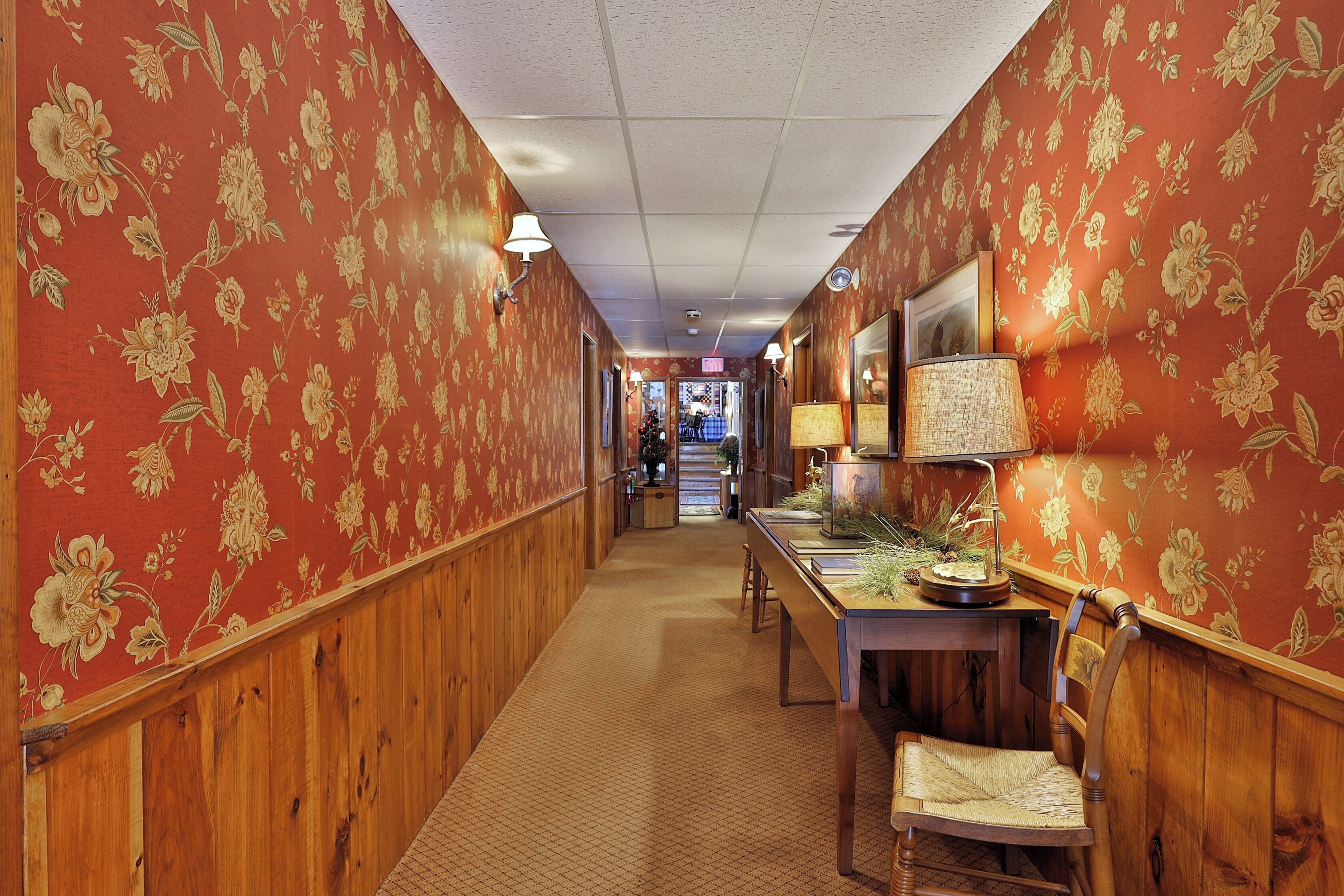 A hallway with floral wallpaper, wooden paneling, a reception desk, and a Christmas tree.
