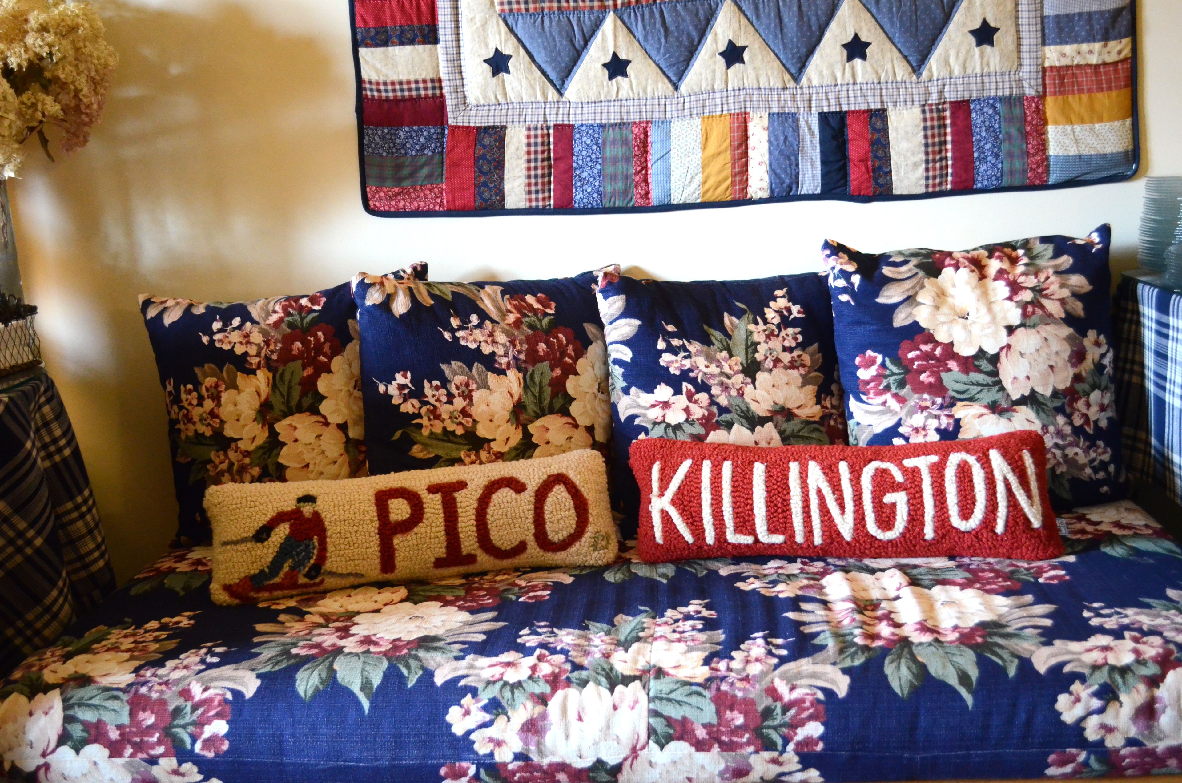 A bed with floral-patterned bedding and two pillows with embroidered text.