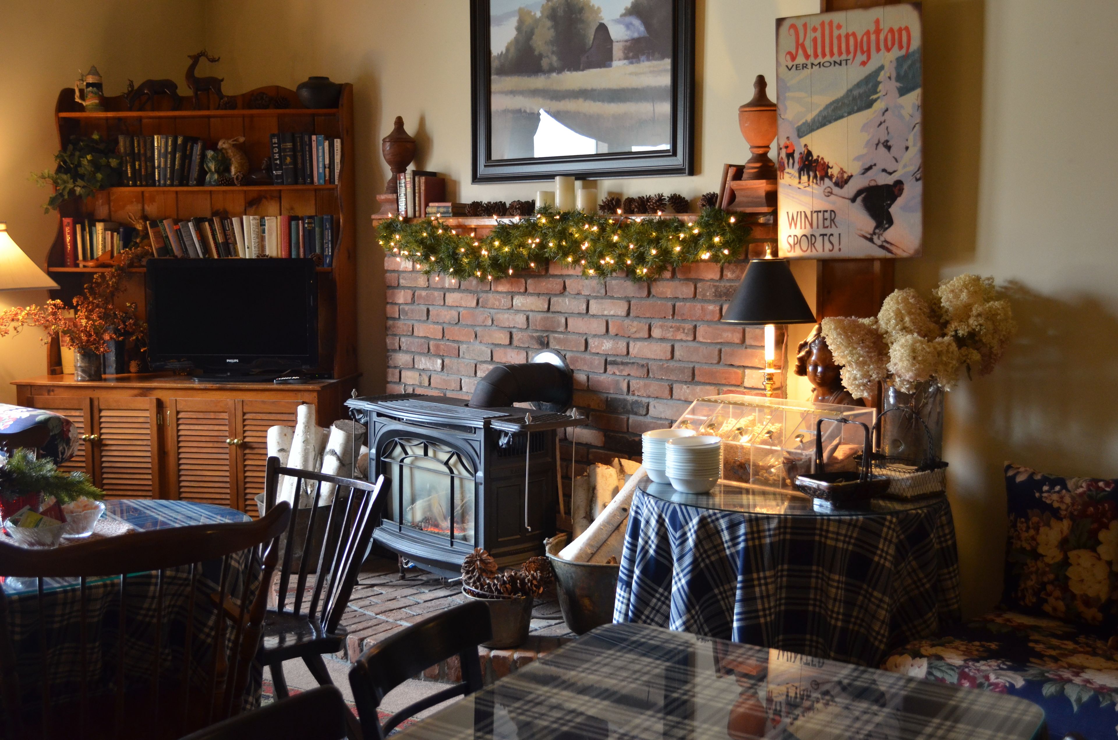 A cozy living room with a brick fireplace, a television, a bookshelf, and a Christmas garland.