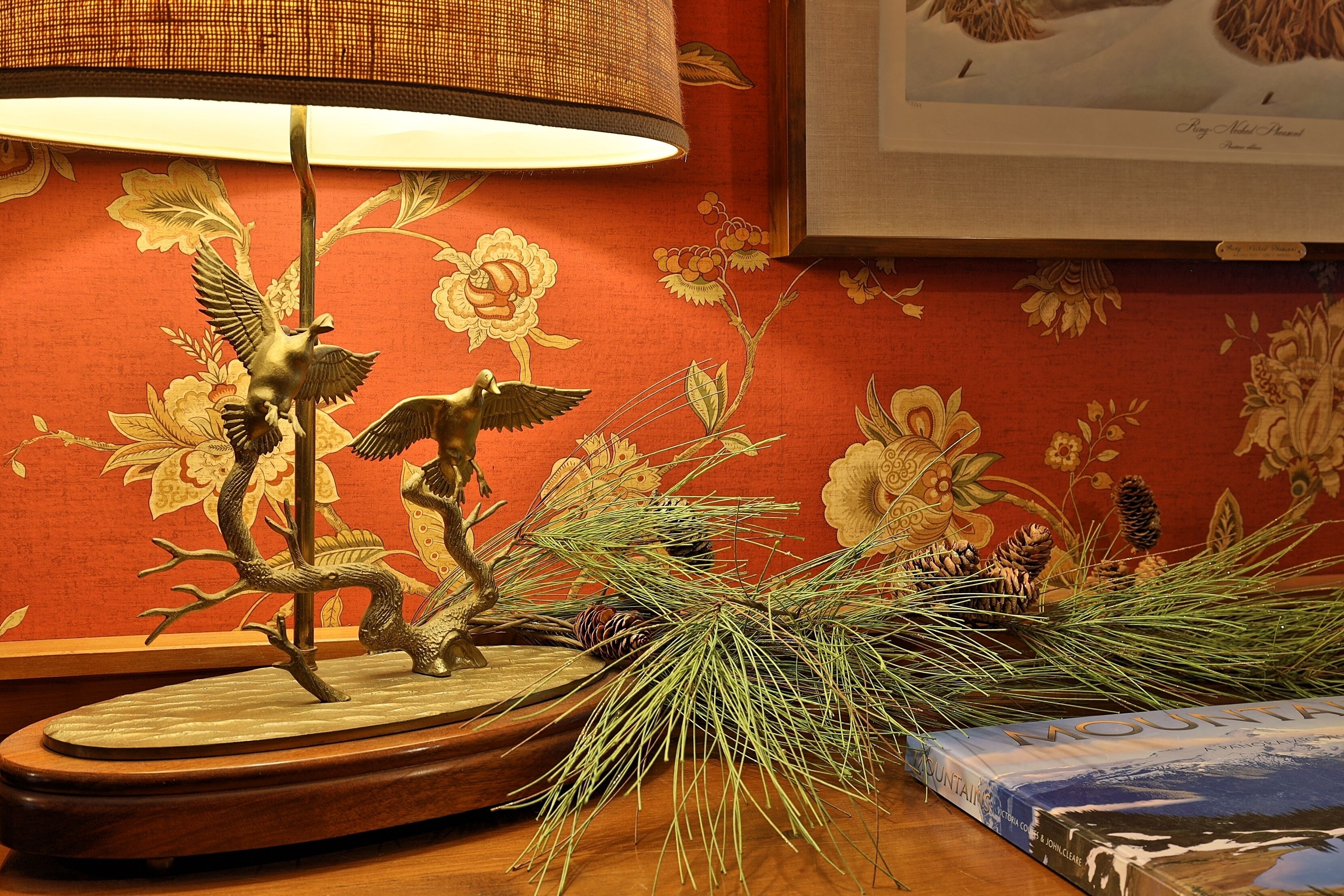 Un tavolo con una lampada, un libro e elementi decorativi tra cui un ramo di pino e una scultura di un uccello.