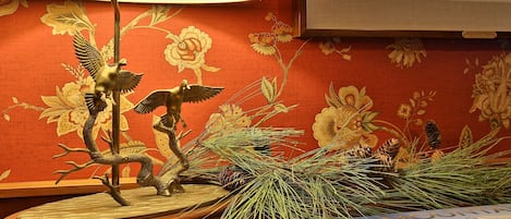 A table with a lamp, a book, and decorative elements including a pine branch and a bird sculpture.