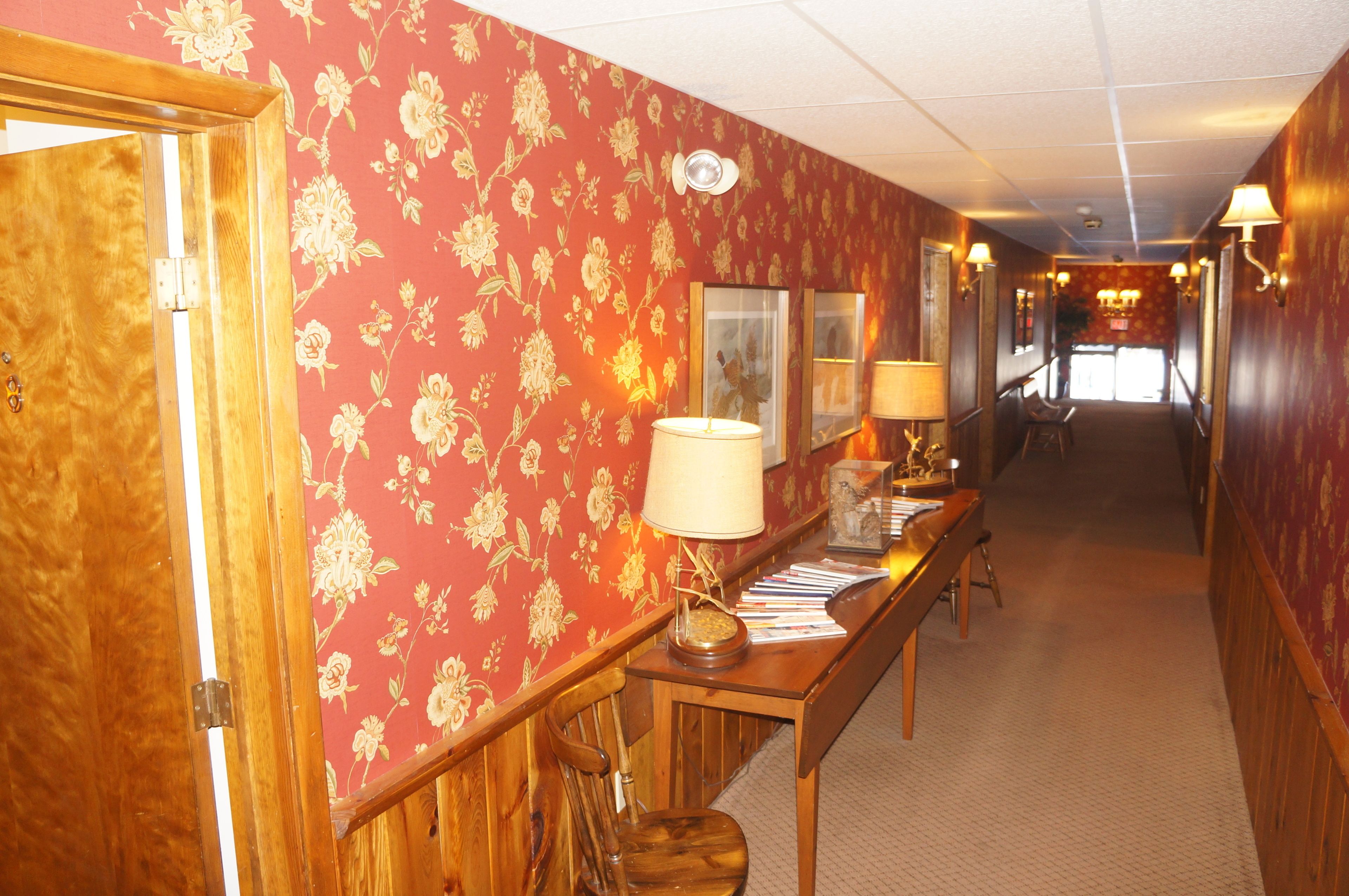 Un pasillo con papel tapiz floral, muebles de madera y lámparas de pared.