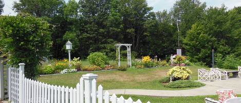 Ein Garten mit weißem Zaun, einer Laube und einer Statue.