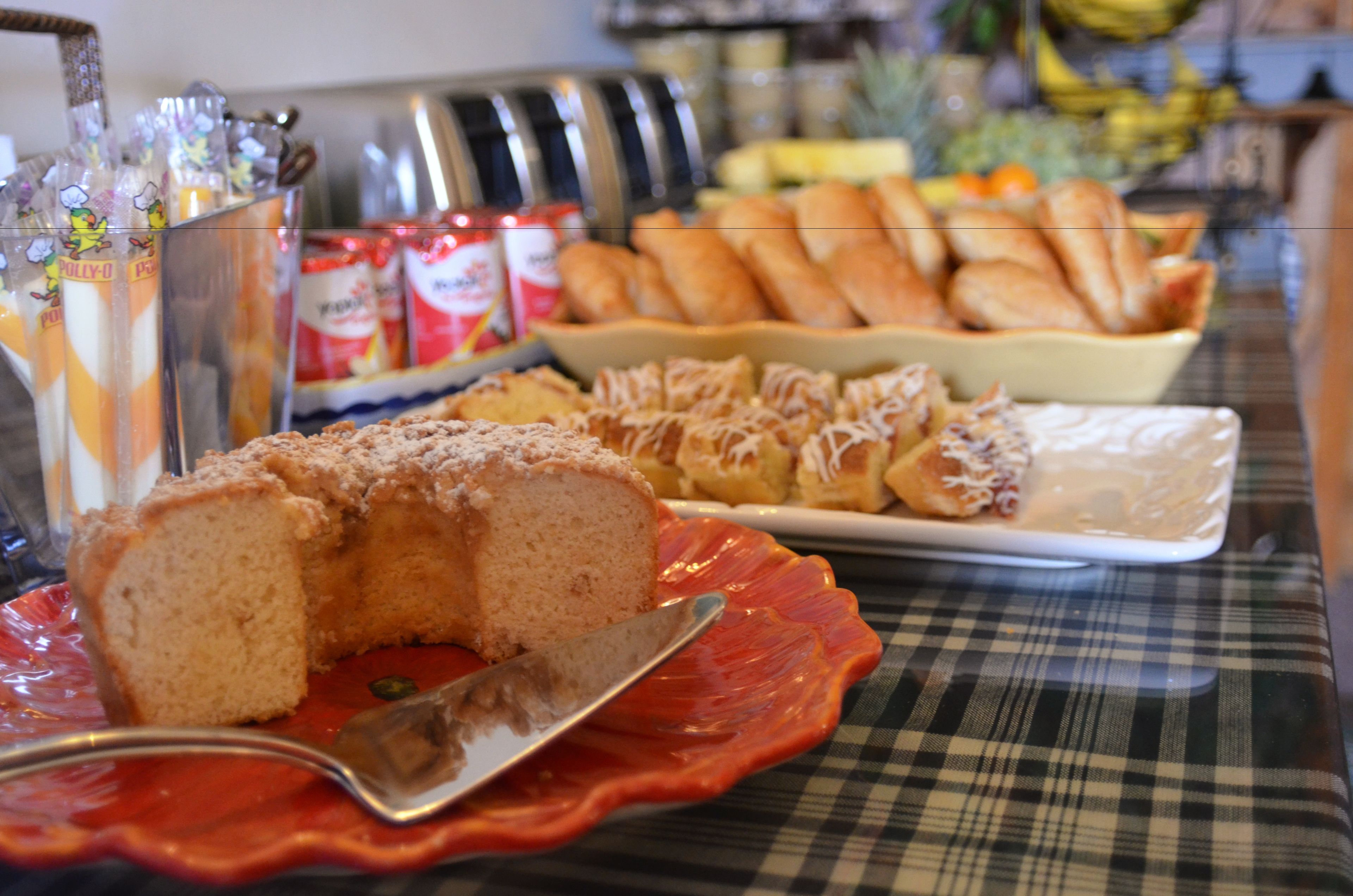 Un bufé de desayuno con diversos pasteles y pan, incluyendo una porción de pastel en un plato rojo.