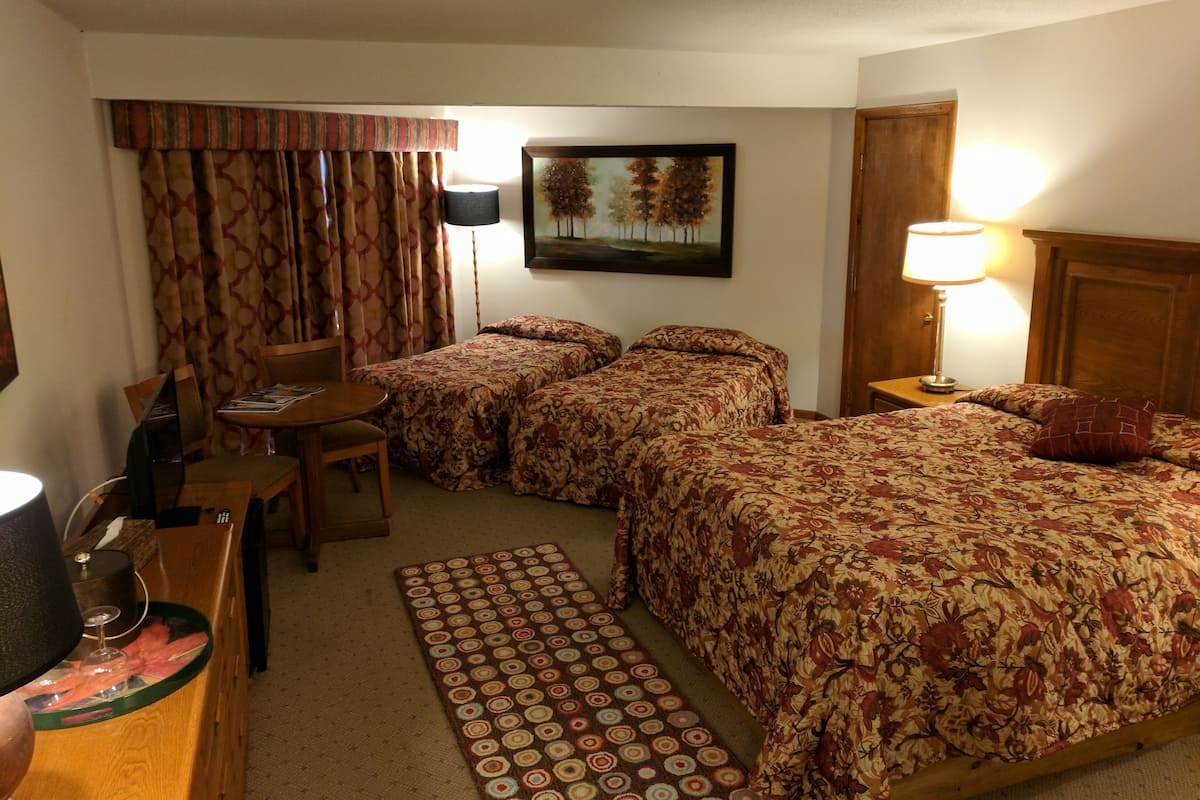 A hotel room with two beds, a desk, a chair, a lamp, and a painting on the wall.