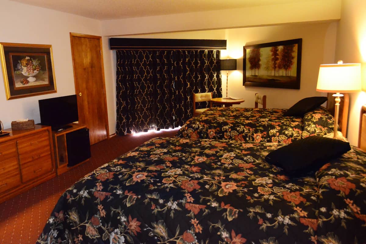 A hotel room with a bed, a desk, a chair, a television, a lamp, and a painting on the wall.