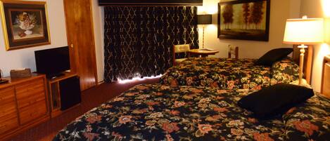 Een hotelkamer met een bed, een bureau, een stoel, een televisie, een lamp en een schilderij aan de muur.