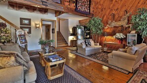 Un salón espacioso con techo alto, vigas de madera, una escalera y un ventanal grande.