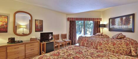 A hotel room with two beds, a TV, a desk with a lamp, and a dresser.