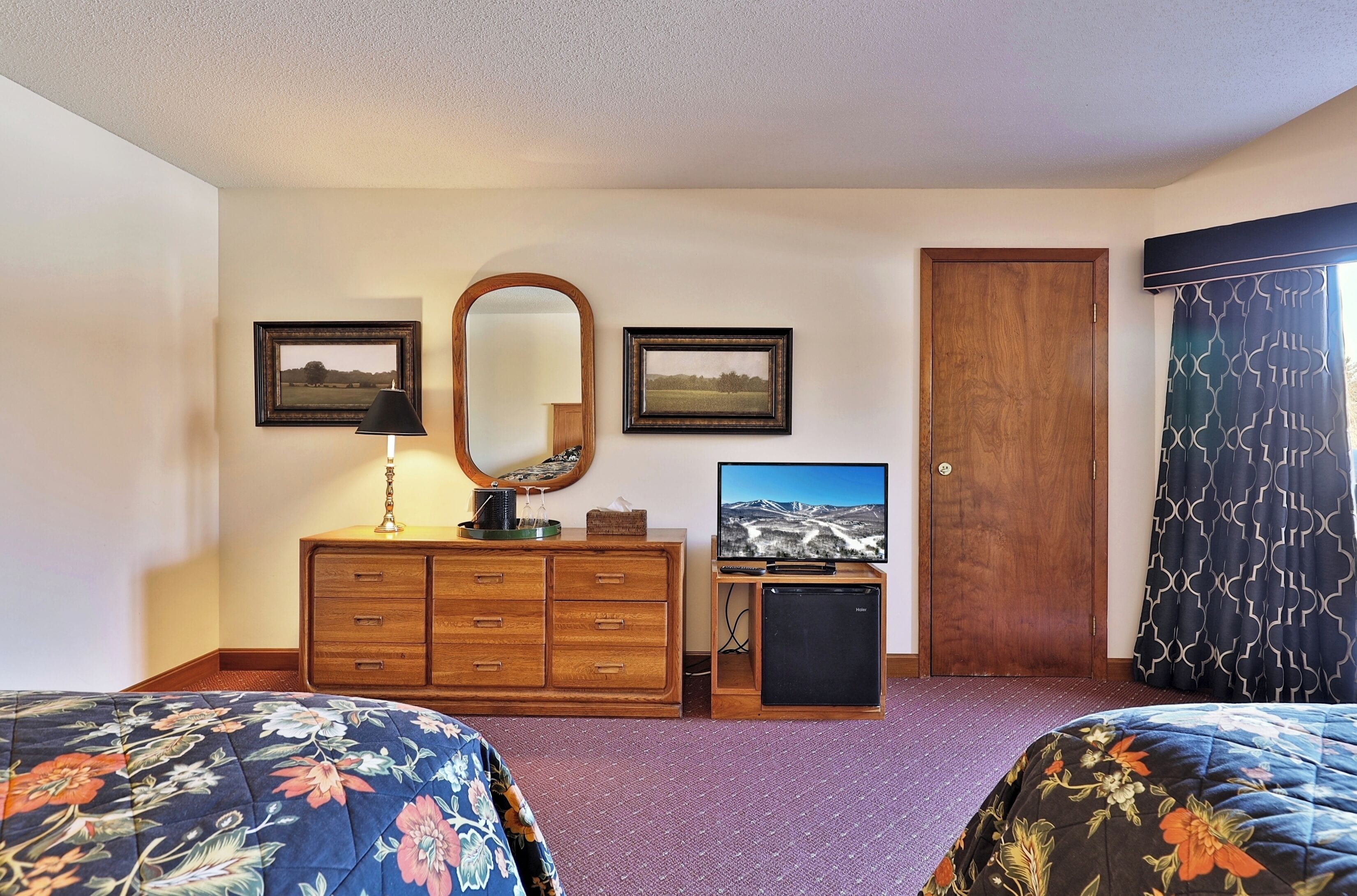Habitación de hotel con dos camas, un aparador de madera, un televisor, un espejo y dos cuadros en la pared.