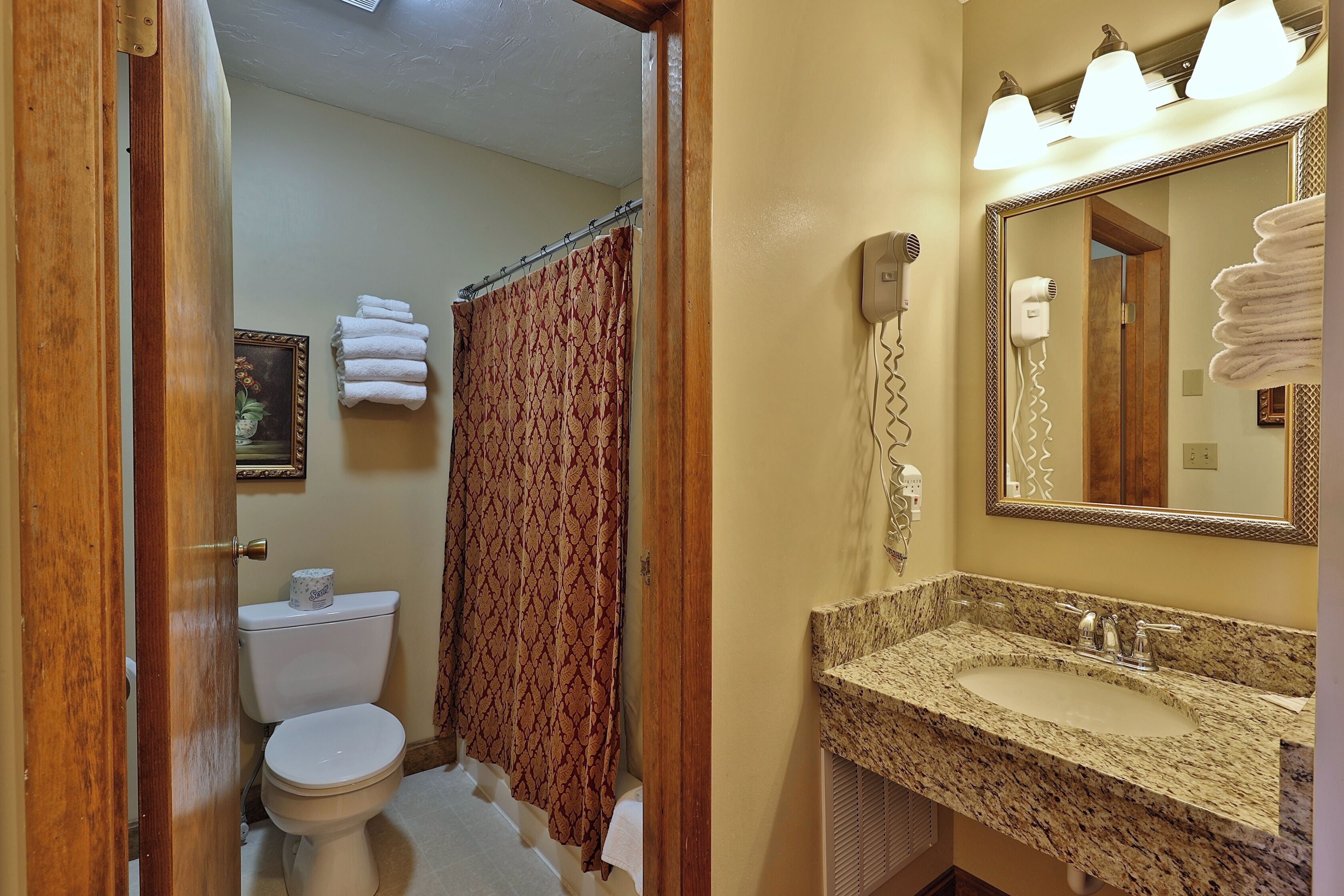 Une salle de bain équipée de toilettes, d’un lavabo, d’un rideau de douche et d’un miroir.