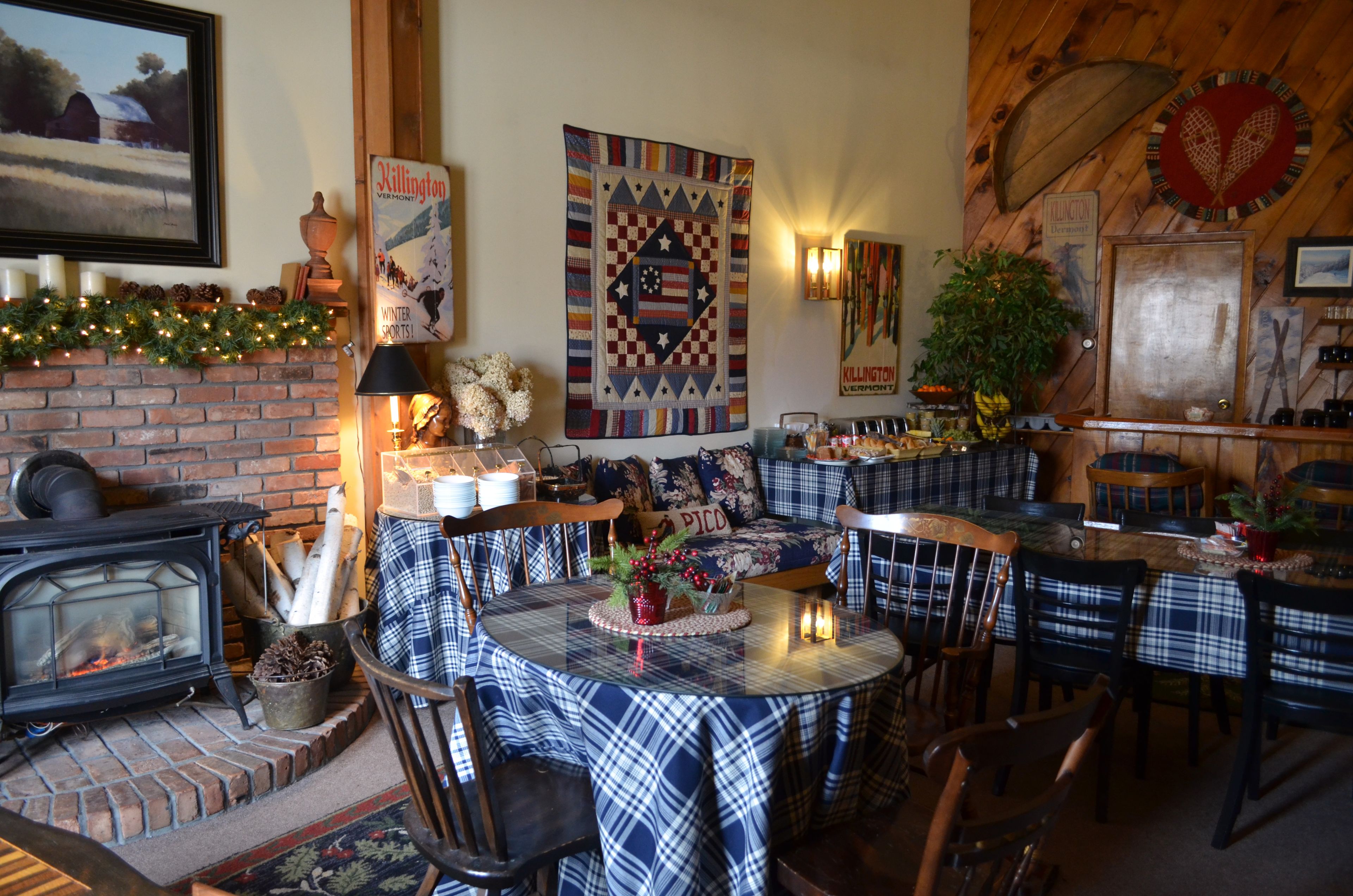 A cozy room with a fireplace, plaid tablecloths, and a quilt on the wall.