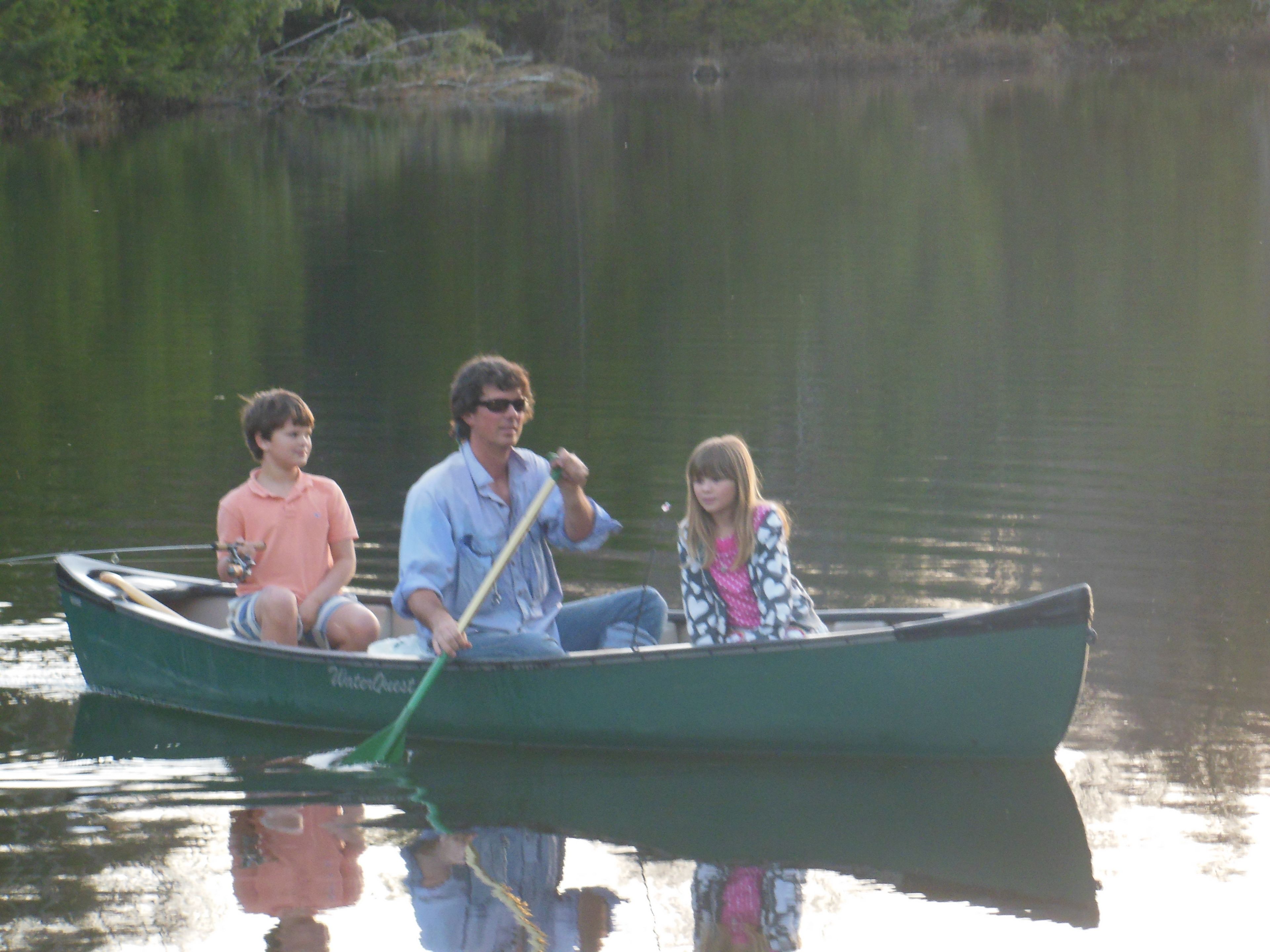 Three people in a green boat on a calm lake.