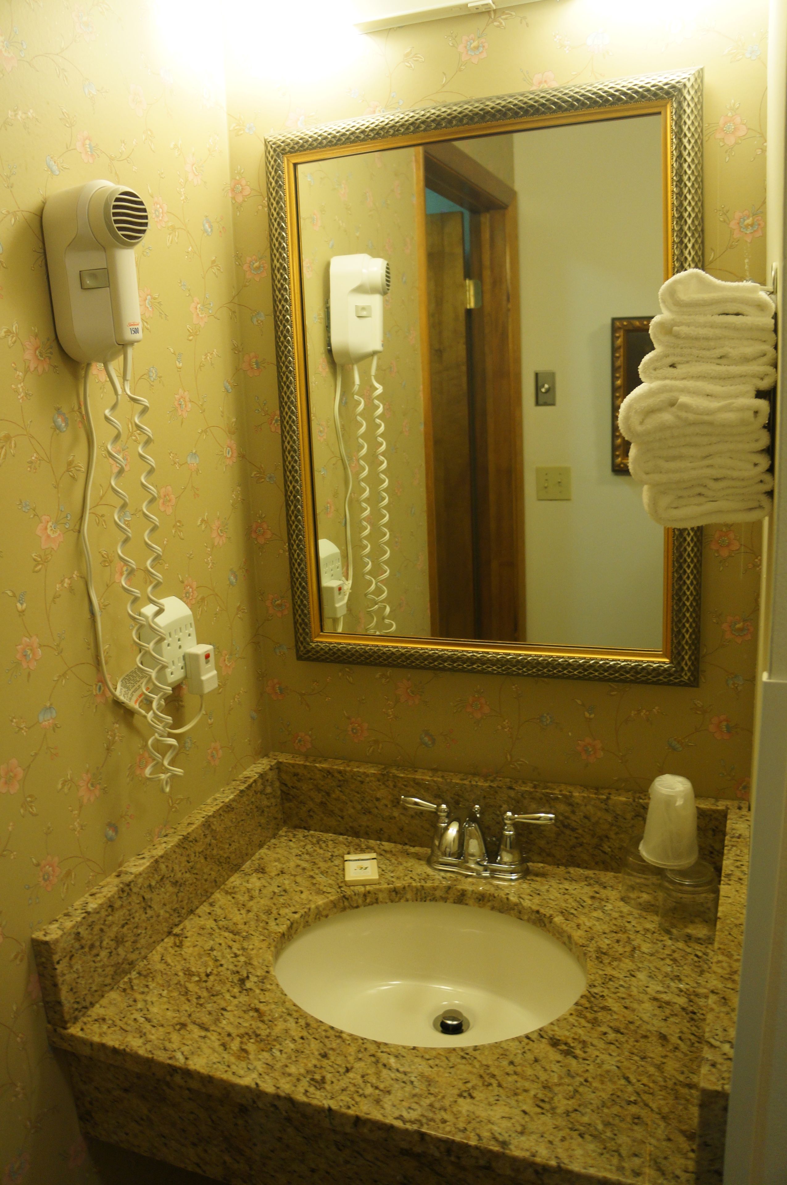 A bathroom with a granite sink, a mirror, a hairdryer, and a stack of towels.