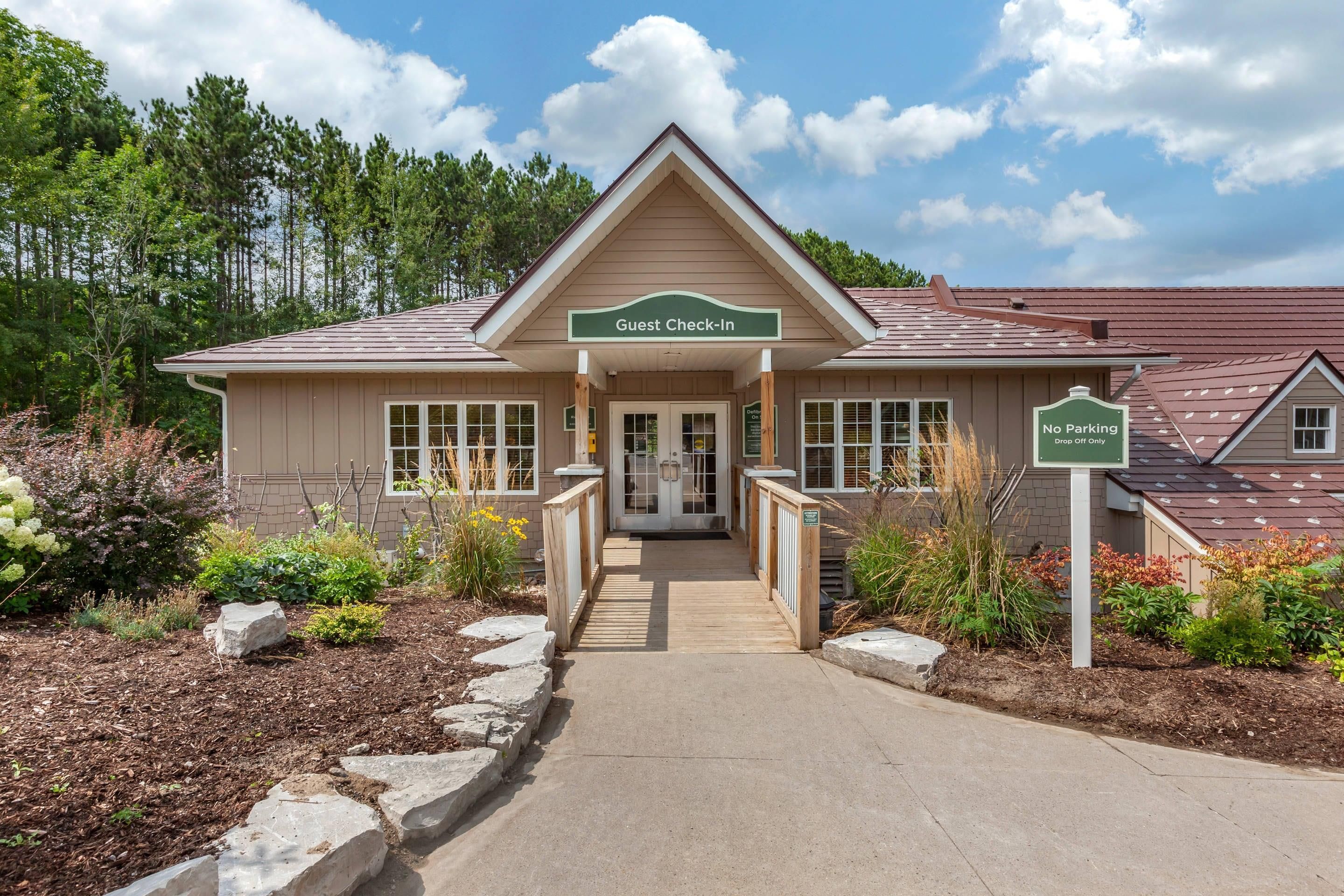 A guest check-in building with a ramp leading to the entrance, surrounded by landscaped gardens and a clear sky.