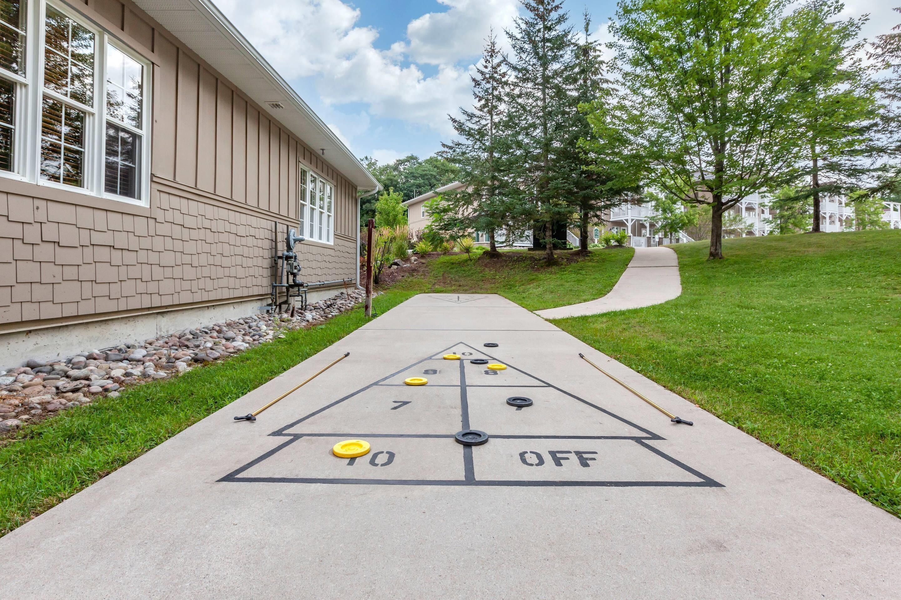 A shuffleboard court adjacent to a building with a brick facade and a paved walkway.