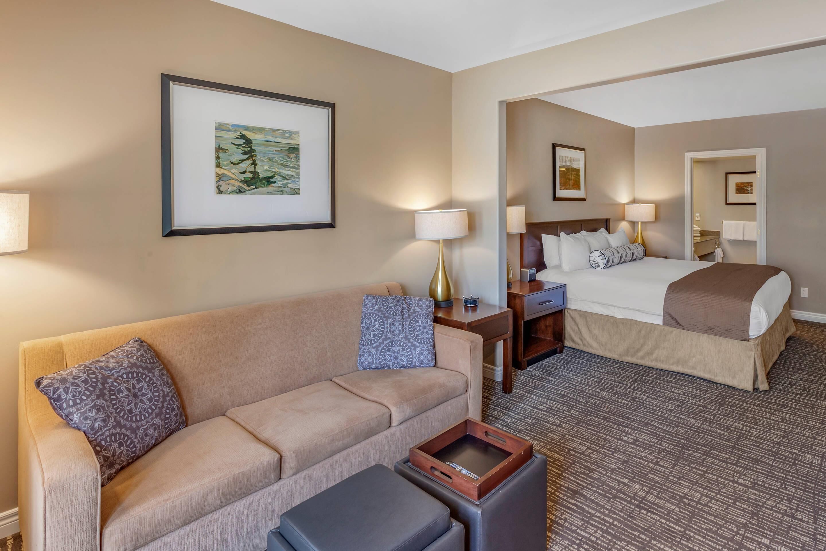 A hotel room with a sofa, a bed, a nightstand, a lamp, and a framed picture on the wall.