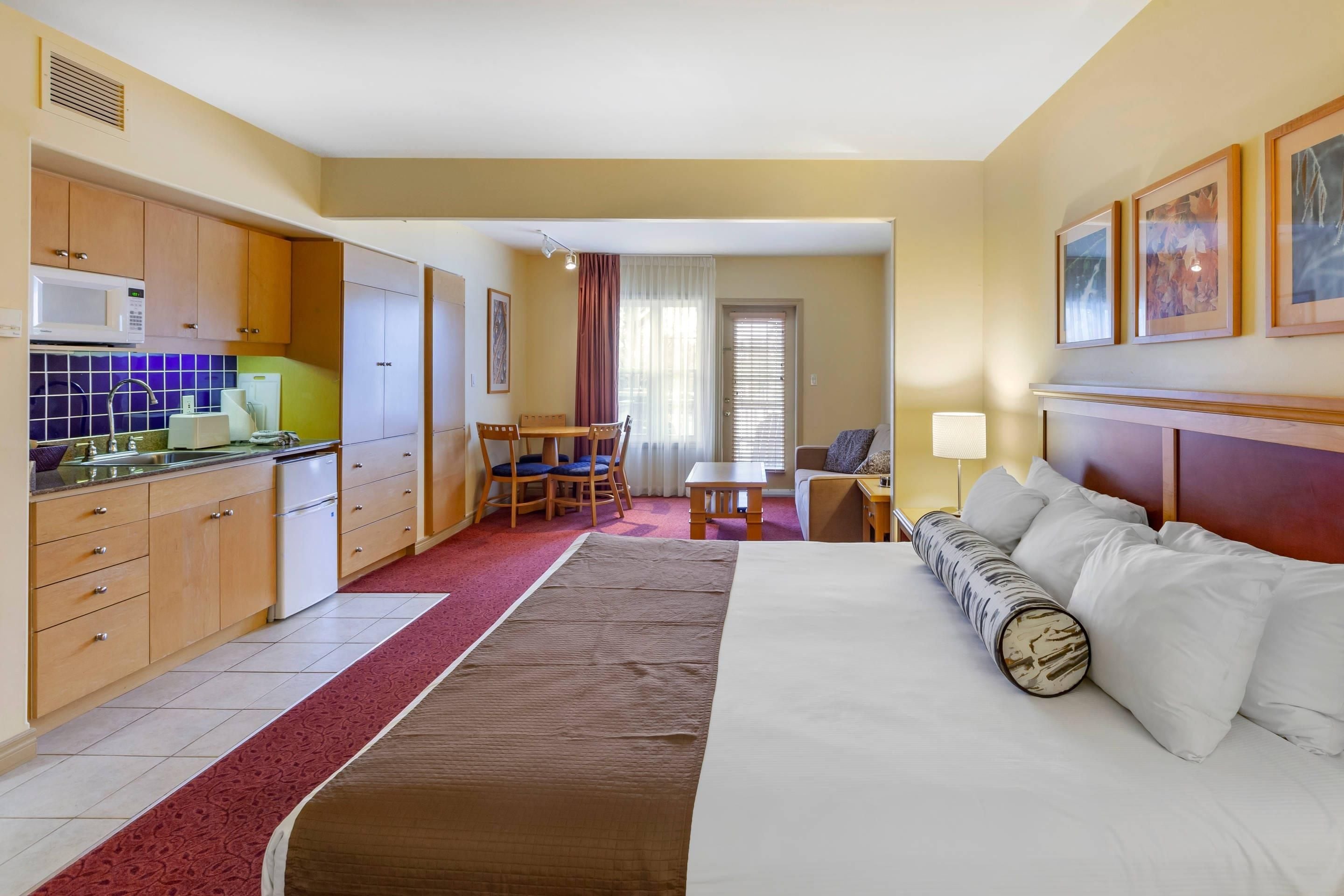 A hotel room with a bed, a desk, a chair, a microwave, a refrigerator, and a window with curtains.