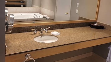 Un bagno con lavandino, due rubinetti, uno specchio e un portasciugamani.