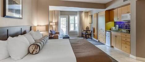A hotel room with a large bed, a desk, a chair, and a kitchenette.