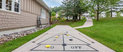 A shuffleboard court with numbered scoring areas and a 'OFF' zone, adjacent to a building with a brick facade and a stone border.