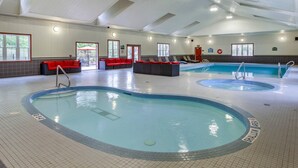 Une piscine intérieure divisée en deux zones distinctes, des espaces détente avec des coussins rouges et un sol carrelé.
