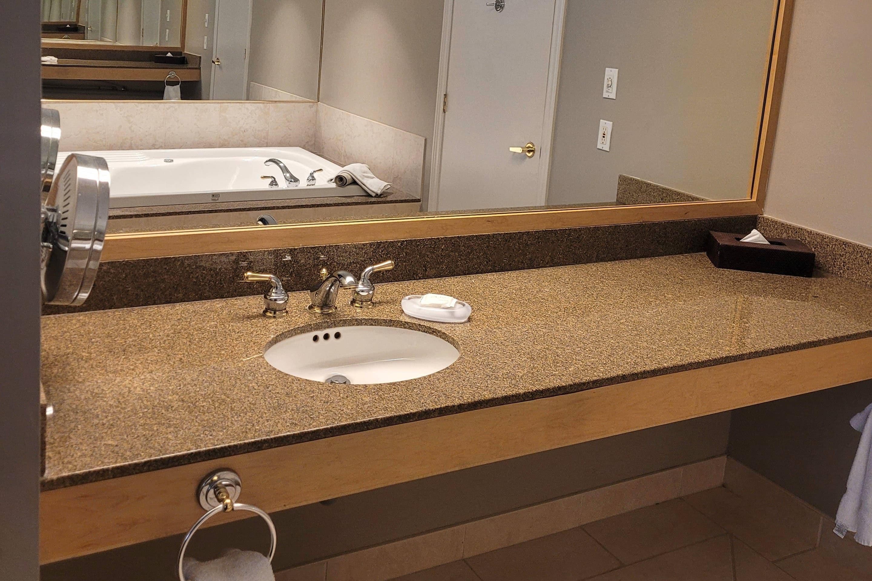 A bathroom with a sink, two faucets, a mirror, and a towel ring.