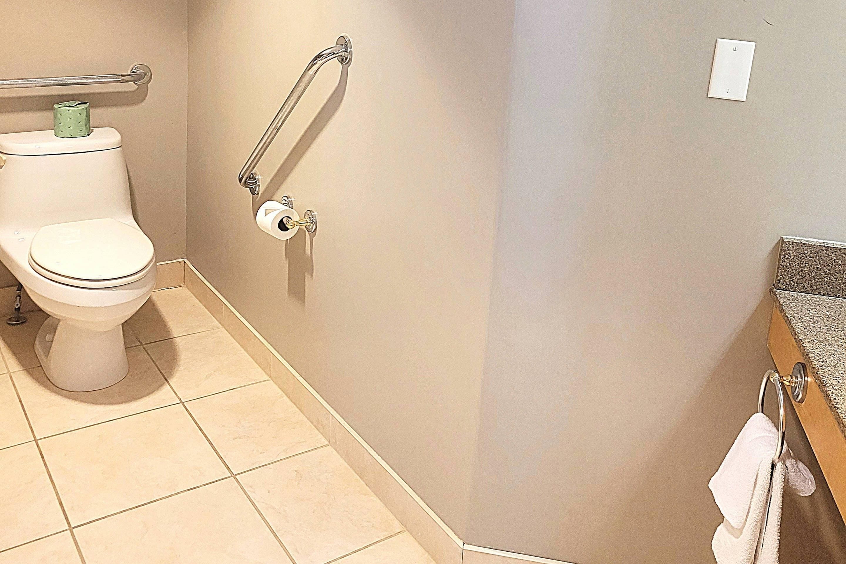 A bathroom with a toilet, grab bars, a towel rack, and a toilet paper holder.